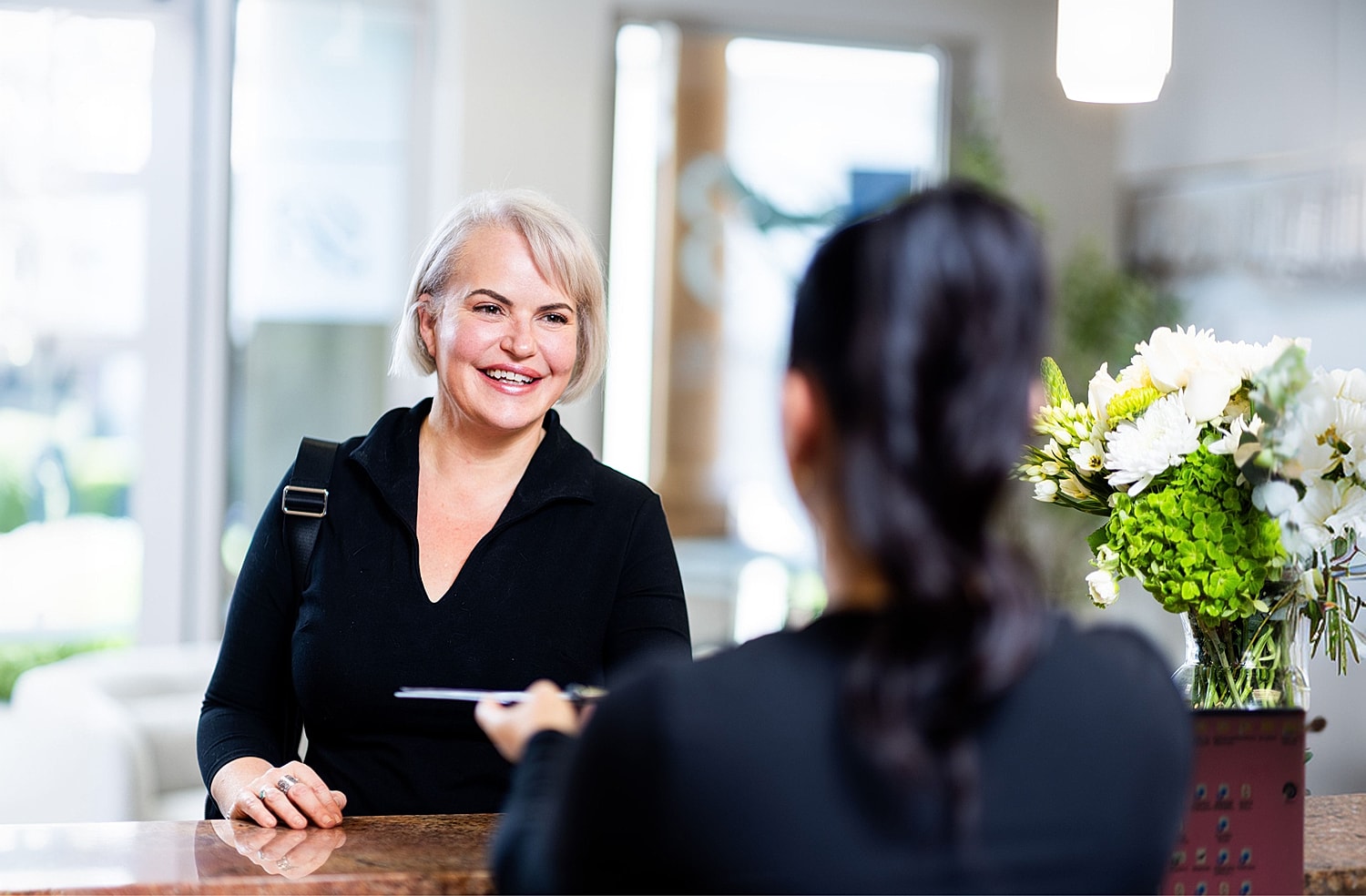 Smiling woman at reception desk interaction.