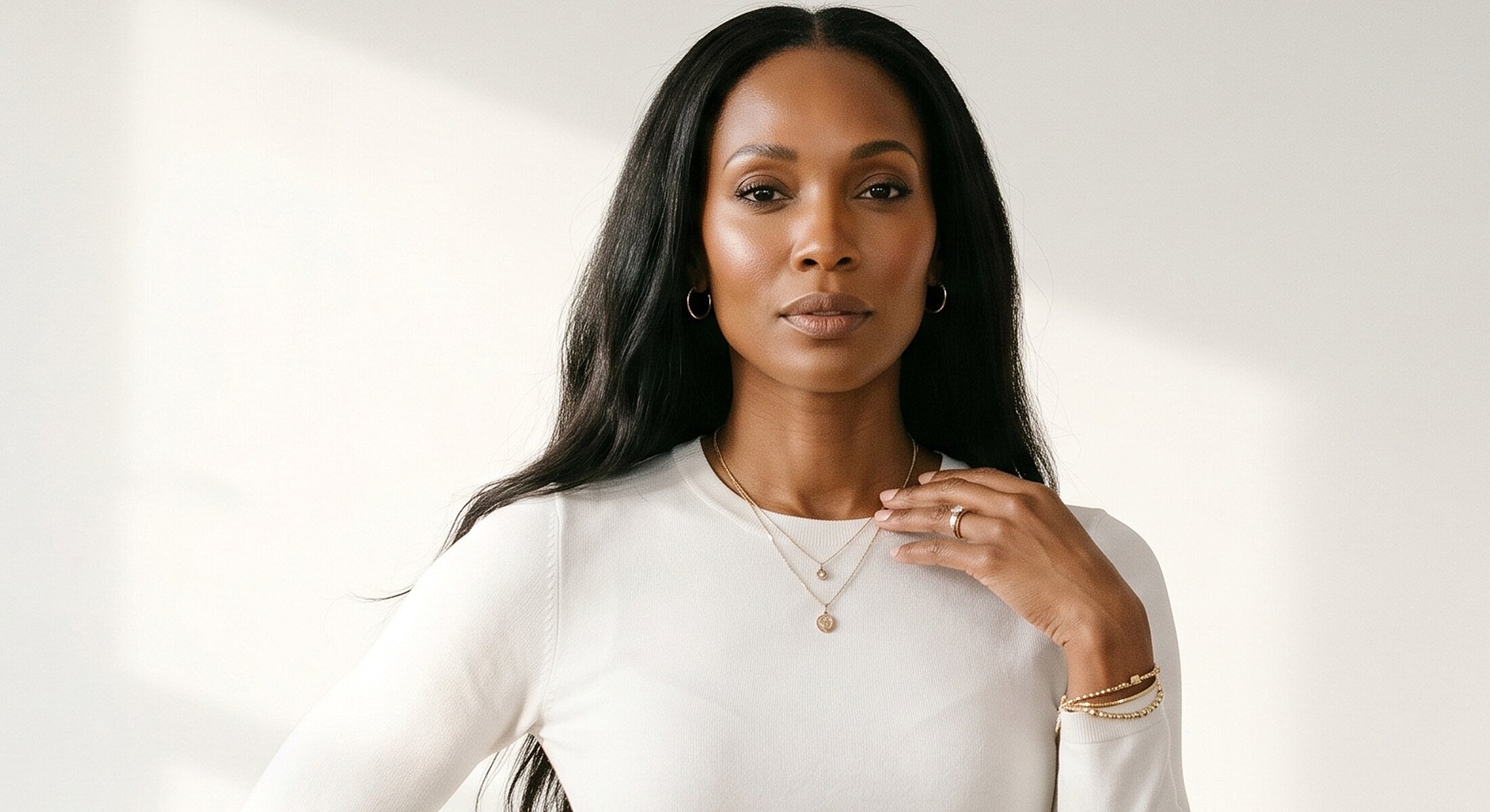 Woman in white top with layered jewelry.