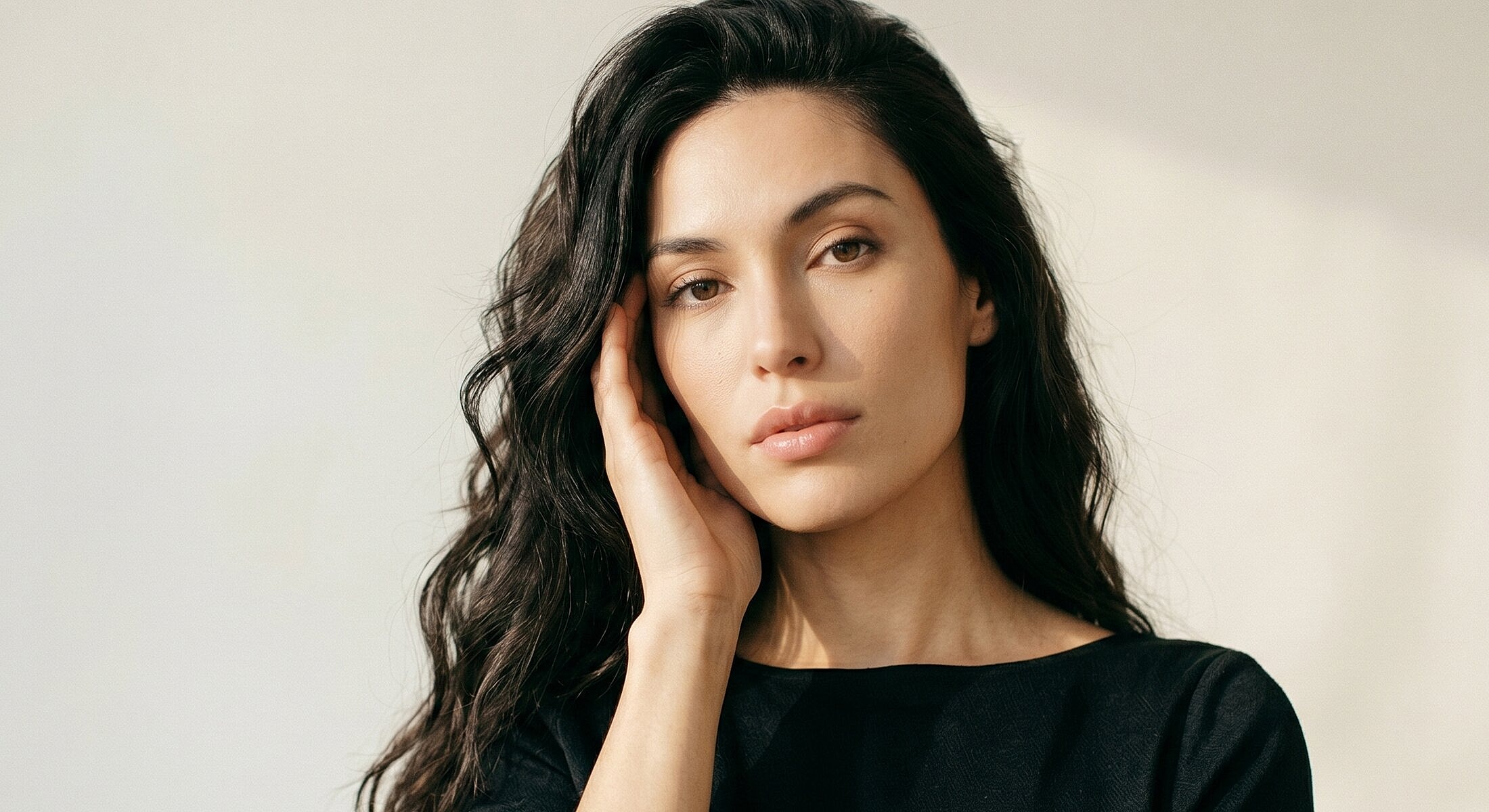 Woman with long hair, gently touching her face.