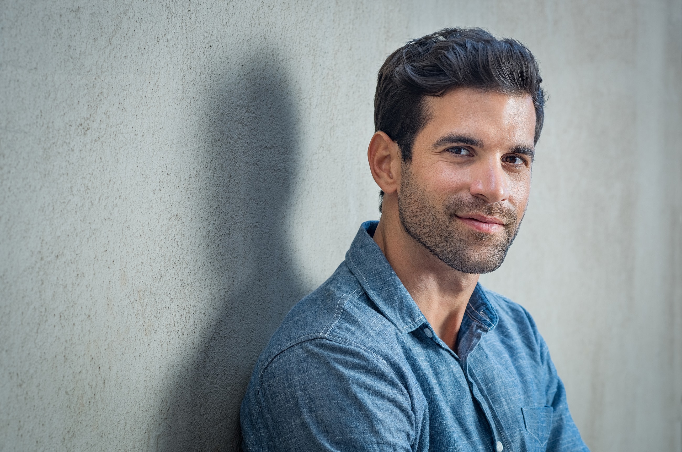 Smiling man in blue shirt against a wall