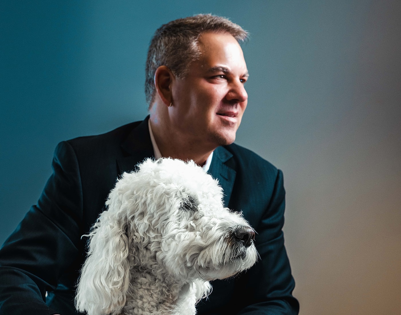 Man in suit sitting beside fluffy dog.